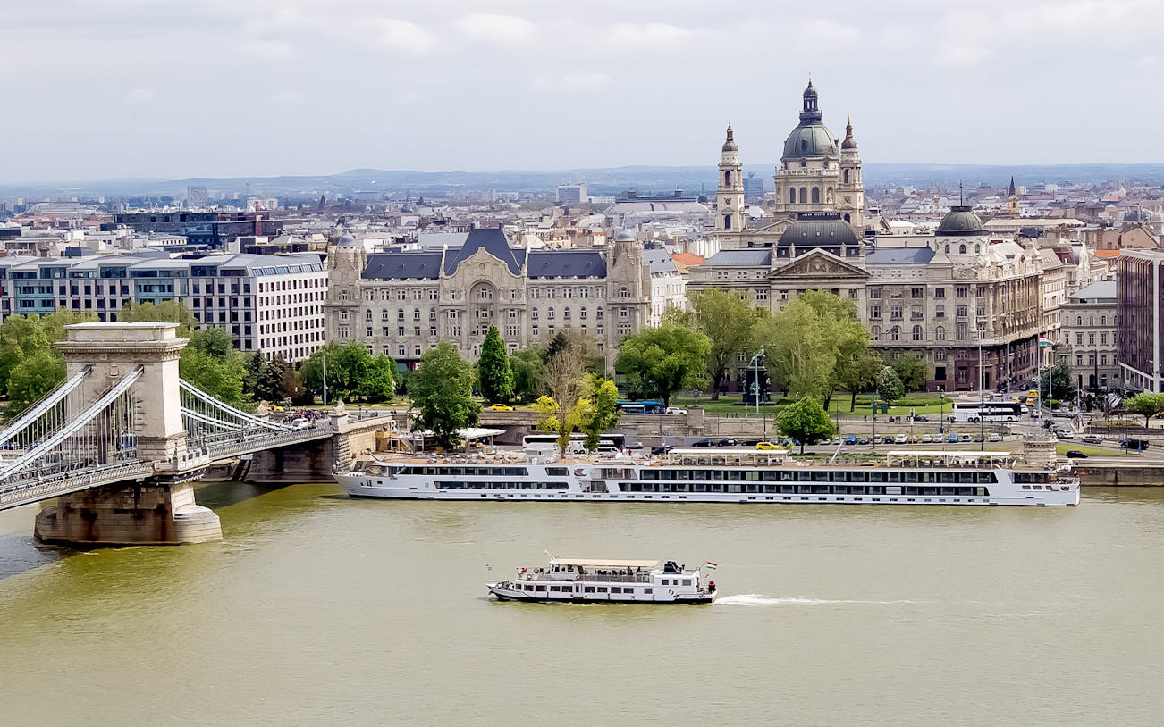Danube River cruise boat passing by Budapest's Chain Bridge and historic buildings.