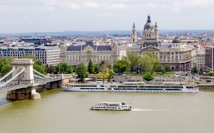 Danube River cruise boat passing by Budapest's Chain Bridge and historic buildings.