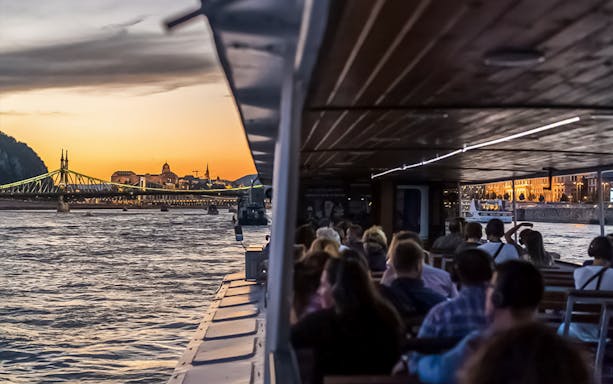 Danube River cruise at sunset with passengers and view of Liberty Bridge, Budapest.