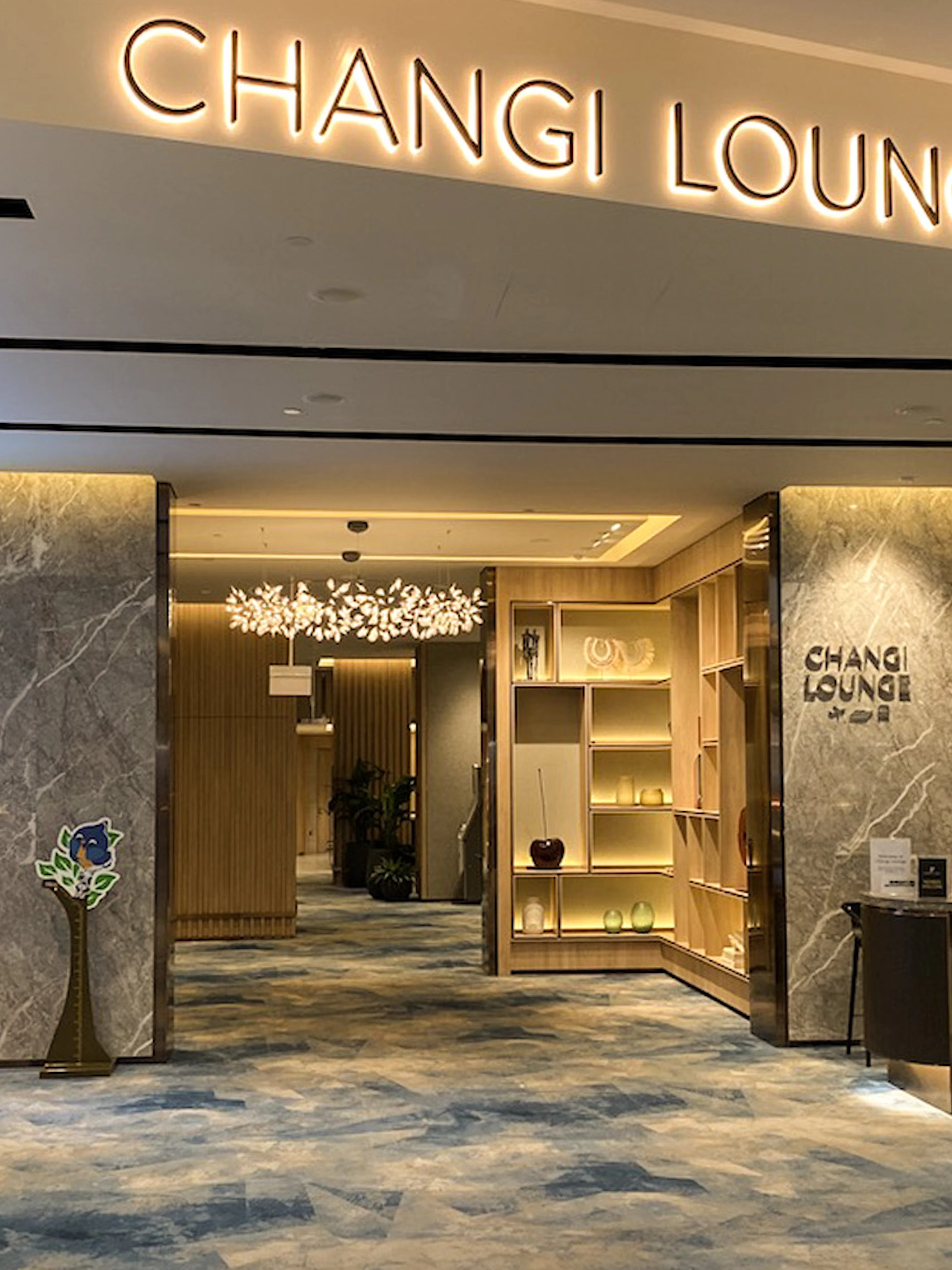 Entrance to Changi Lounge at Singapore Airport with reception desk and signage.