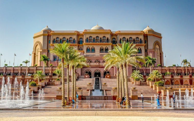 Emirates Palace facade with palm trees and fountains, Abu Dhabi sightseeing tour.