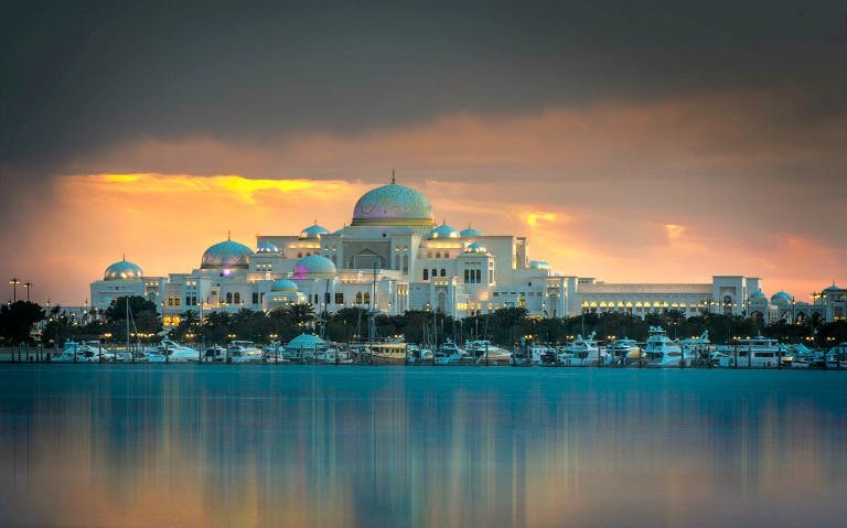 Abu Dhabi skyline with Emirates Palace at sunset, reflecting on the water.