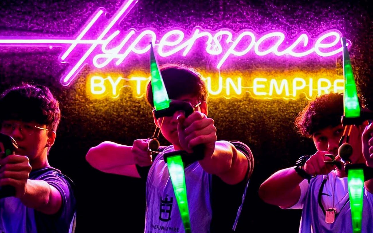 Participants aiming bows at FunEmpire with neon "Hyperspace" sign in background.