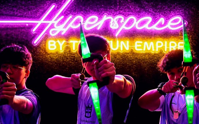 Participants aiming bows at FunEmpire with neon "Hyperspace" sign in background.