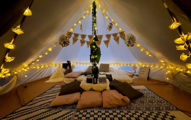 Glamping tent interior with cozy bedding, decorative lights, and cushions at a Glamping Society.