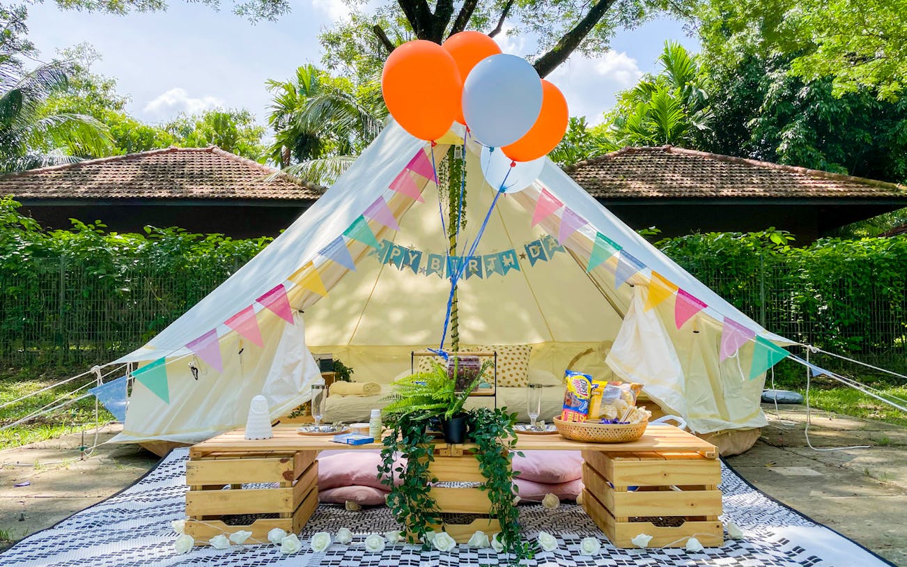 Glamping tent setup with colorful bunting and balloons in a lush outdoor setting.