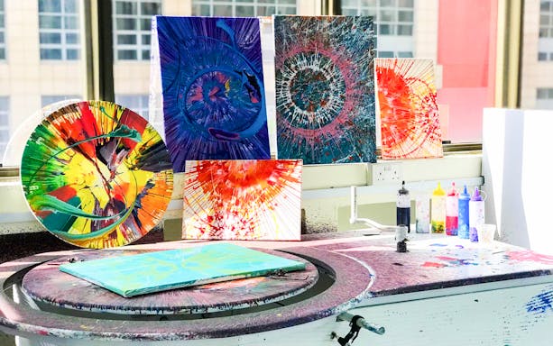 Spin Paint House artworks displayed on a table with colorful paint bottles.
