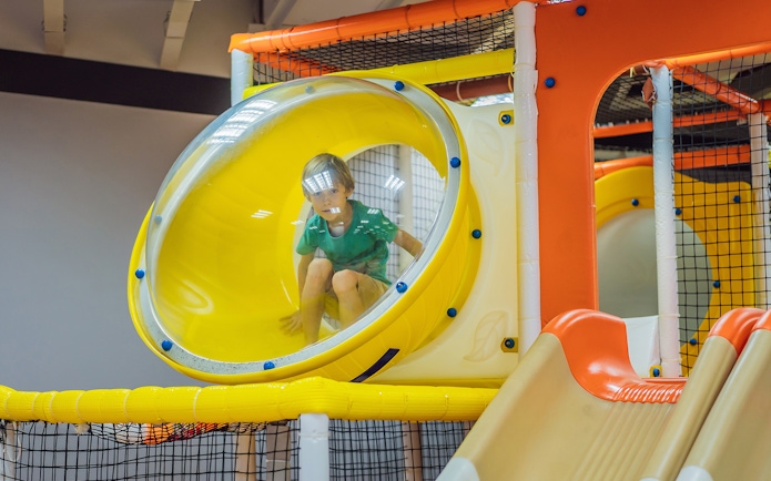 Child playing in a yellow tube slide at T-Play Khatib indoor playground.