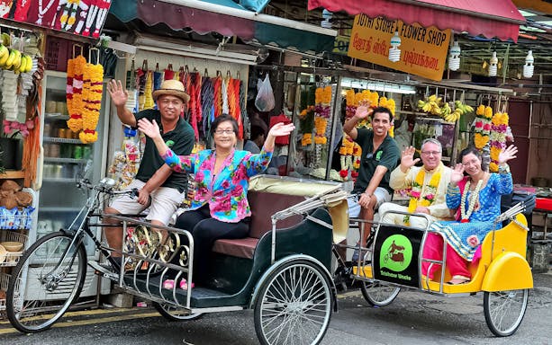 Trishaw tour group waving in front of a flower shop in Singapore.