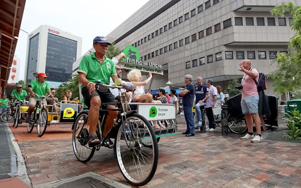 Trishaw riders in green shirts leading a guided tour in Singapore's Albert Mall Trishaw Park.