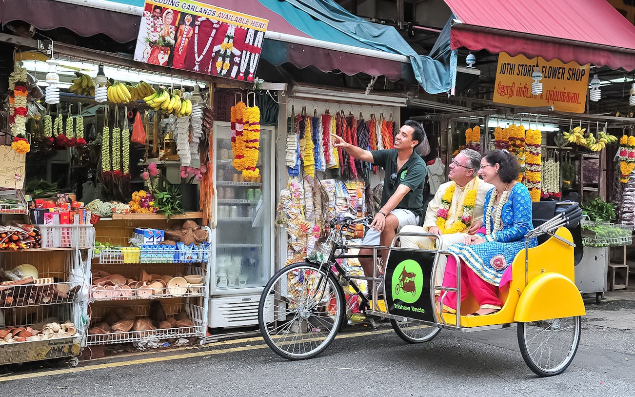 Trishaw tour guide pointing at flower shop in Singapore's vibrant market.