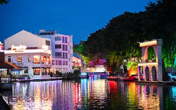 Melaka River Cruise with illuminated riverside buildings and colorful reflections.