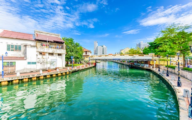 Melaka River with historic buildings and a bridge under a clear blue sky.