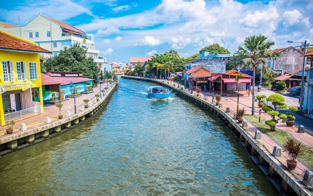 Melaka River Cruise boat navigating past colorful riverside buildings.