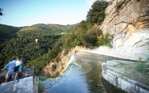 Visitors overlooking waterfall and lush landscape at Villa Gregoriana, Tivoli, Italy.