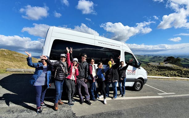 Group enjoying scenic view on Napier and Hawkes Bay tour with tour van in background.