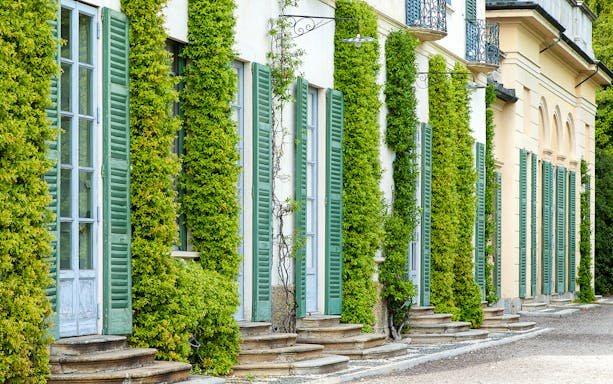 Villa e Collezione Panza facade with green shutters and climbing plants.