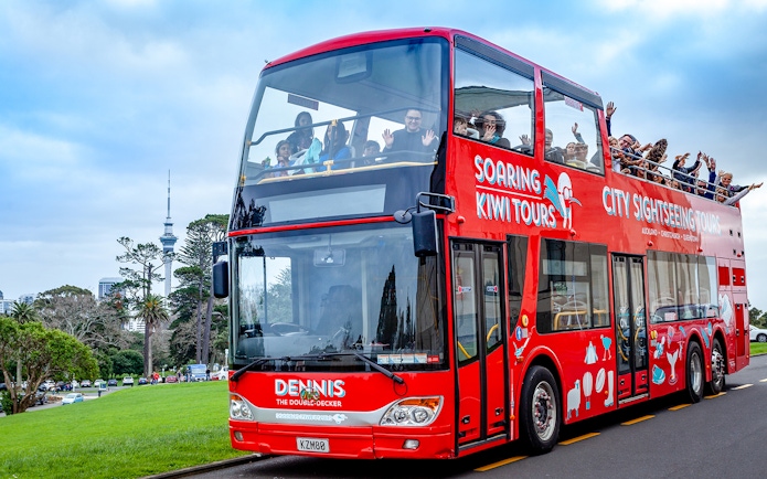 Red double-decker bus on Auckland city tour with Sky Tower in background.