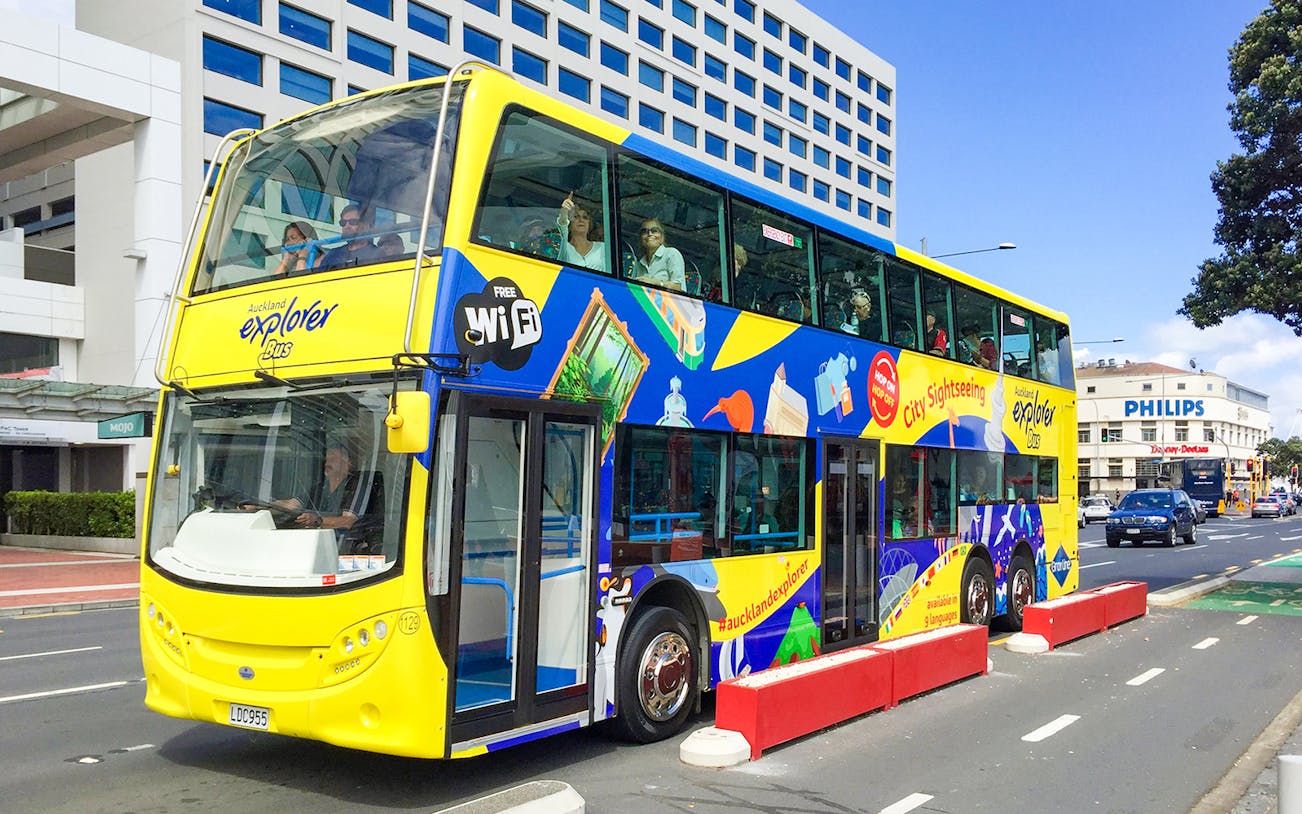 Auckland Explorer Bus at Viaduct Harbour with city skyline in background.