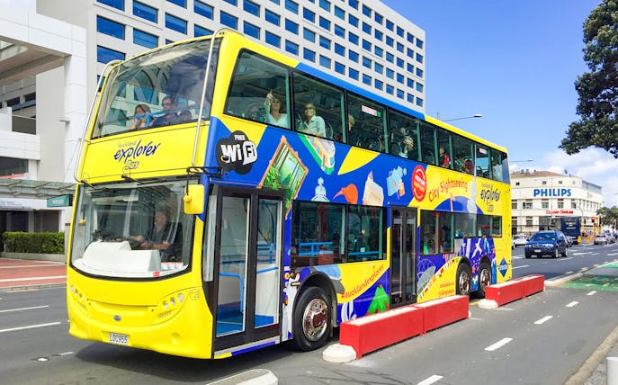 Auckland Explorer Bus at Viaduct Harbour with city skyline in background.