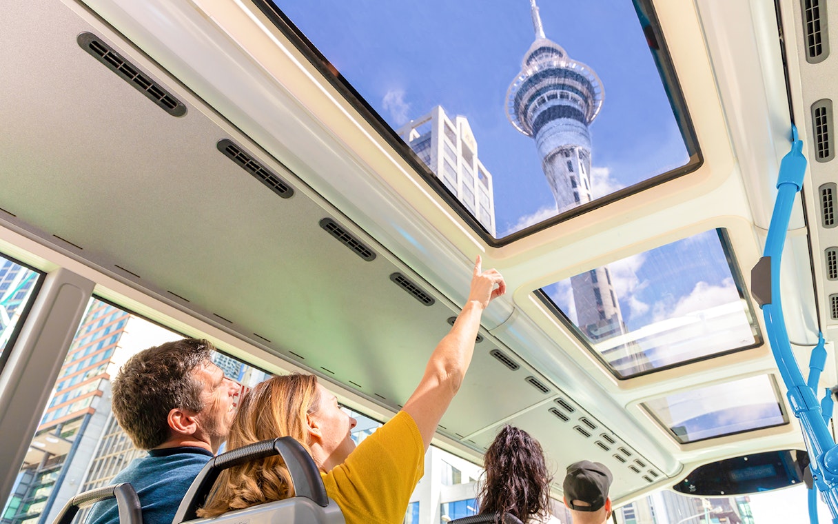 Auckland Explorer Bus passengers view Sky Tower through glass roof.