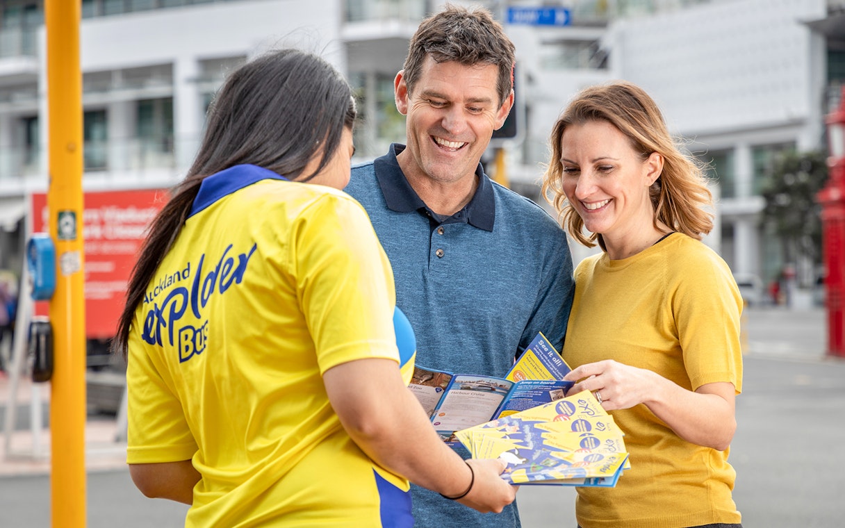 Auckland Explorer Bus staff assisting tourists with city tour brochures.