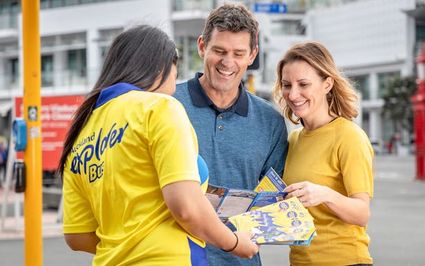 Auckland Explorer Bus staff assisting tourists with city tour brochures.