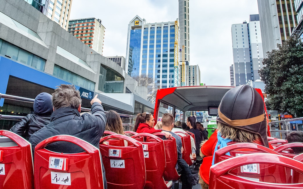Open-top bus tour in Auckland city with passengers viewing skyscrapers.