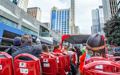 Open-top bus tour in Auckland city with passengers viewing skyscrapers.