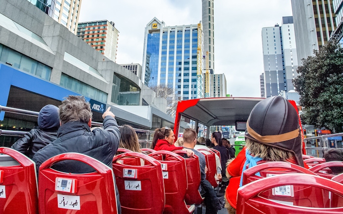 Open-top bus tour in Auckland city with passengers viewing skyscrapers.