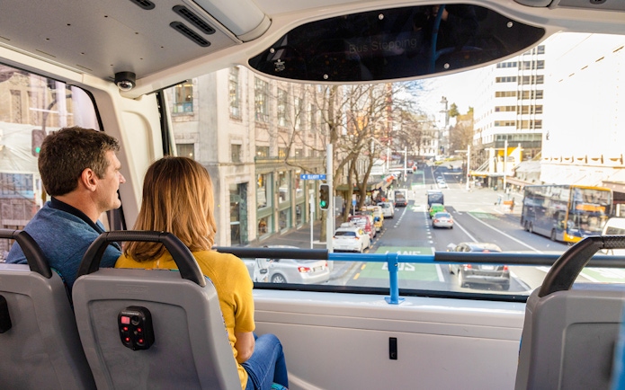 Passengers on Auckland Explorer Bus viewing city street.