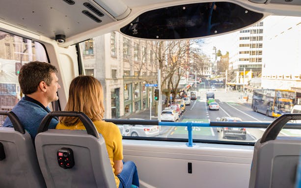 Passengers on Auckland Explorer Bus viewing city street.