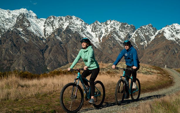 Cyclists on a trail with mountain views during Queenstown winery bike tour.
