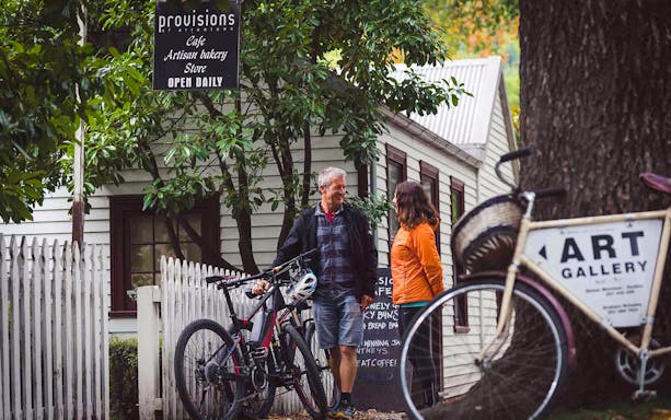 Couple with bikes outside Provisions Cafe in Arrowtown on Queenstown winery tour.