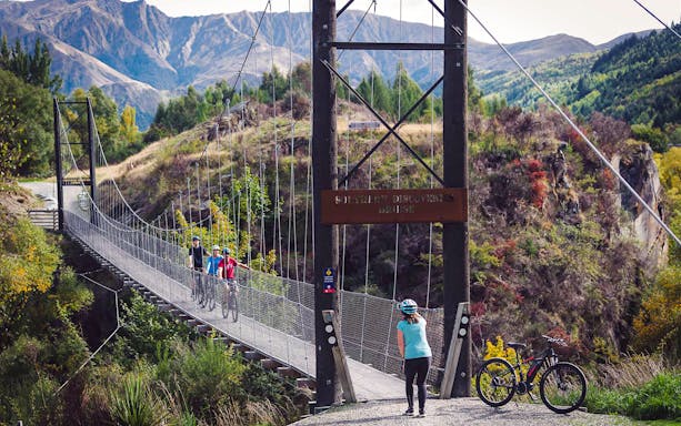 Cyclists crossing a suspension bridge on a winery tour near Queenstown.