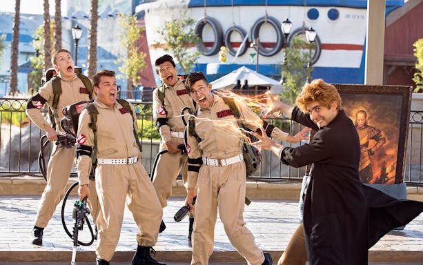 Ghostbusters characters posing with a visitor at a theme park attraction.