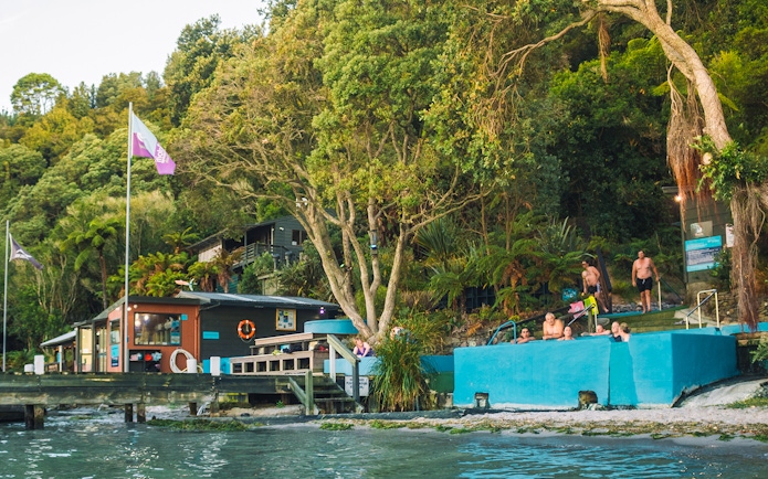 Kayakers relaxing in Manupirua Hot Pools on Lake Rotoiti, surrounded by lush greenery.