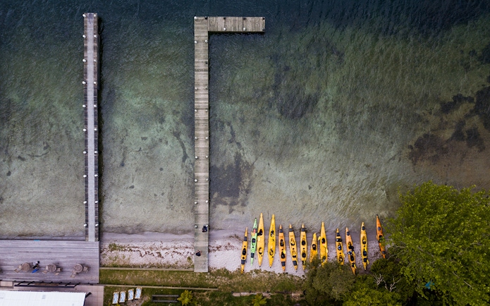 Kayaks lined up on Lake Rotoiti shore near wooden pier, New Zealand.