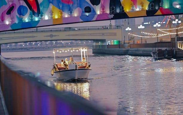Private boat tour on Khalid Lagoon under a colorful bridge at dusk.