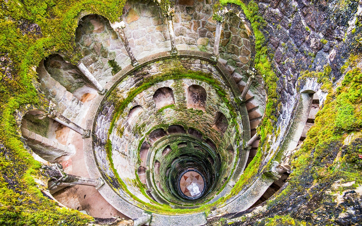 Quinta da Regaleira's Initiation Well in Sintra, Portugal, with moss-covered spiral staircase.