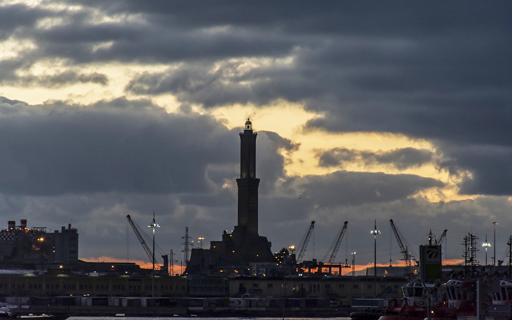 Genoa's Lighthouse at sunset with cranes in the harbor.