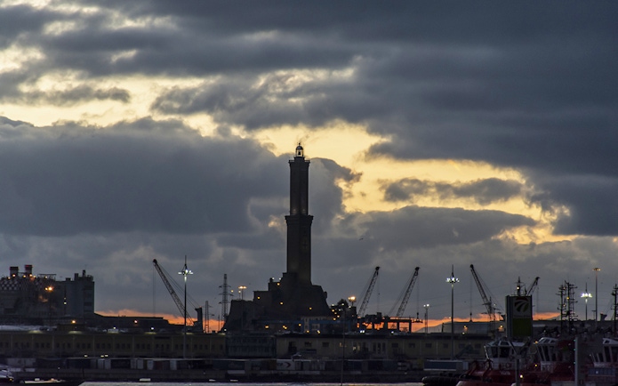 Genoa's Lighthouse at sunset with cranes in the harbor.
