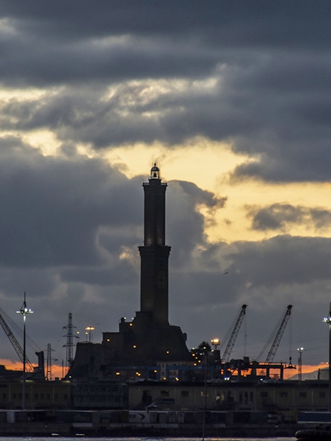 Genoa's Lighthouse at sunset with cranes in the harbor.