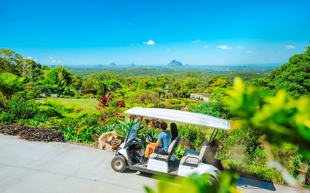 Golf cart driving through Maleny Botanic Gardens with scenic mountain view.