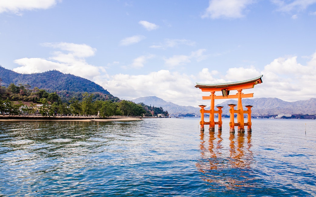 Torii gate at Itsukushima Shrine in Hiroshima, Japan, with mountains in the background.