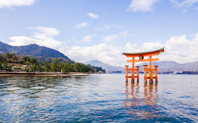 Torii gate at Itsukushima Shrine in Hiroshima, Japan, with mountains in the background.