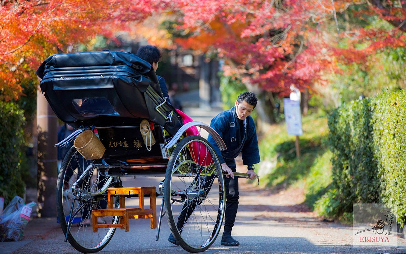 Rickshaw driver preparing for a ride in Arashiyama, Kyoto, with autumn foliage.