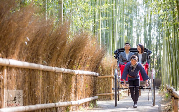 Tour guide pulling a rickshaw with tourists on board, exploring the scenic beauty of Kyoto Arashiyama