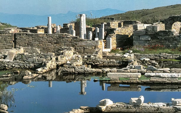 Ancient ruins of Delos with stone columns and reflections in water, viewed from Mykonos.