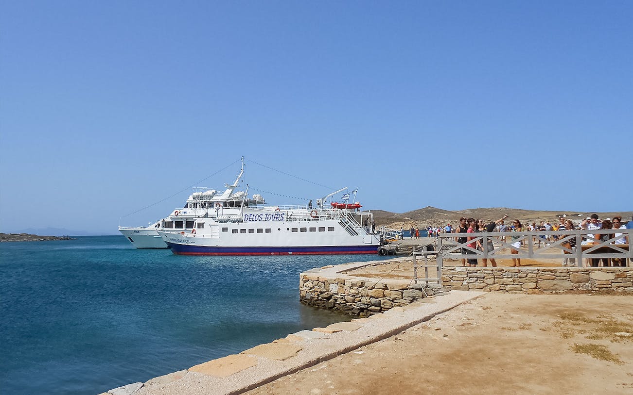 Ferry docked at Delos with tourists disembarking, part of Mykonos guided tour.